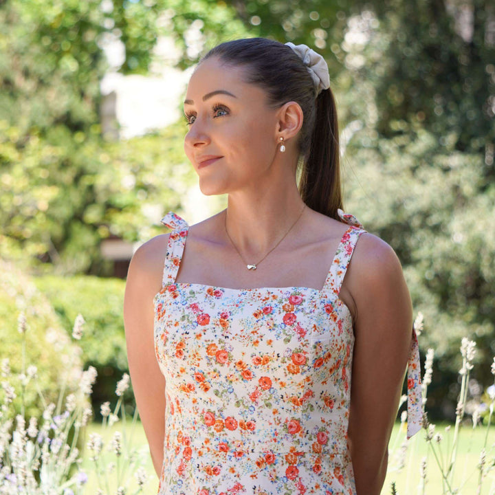 Woman in a floral dress standing outdoors with greenery in the background